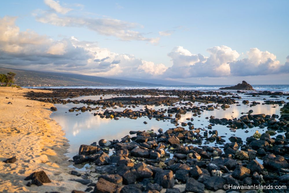 Rocky beach with tide pools under a cloudy sky at sunset.