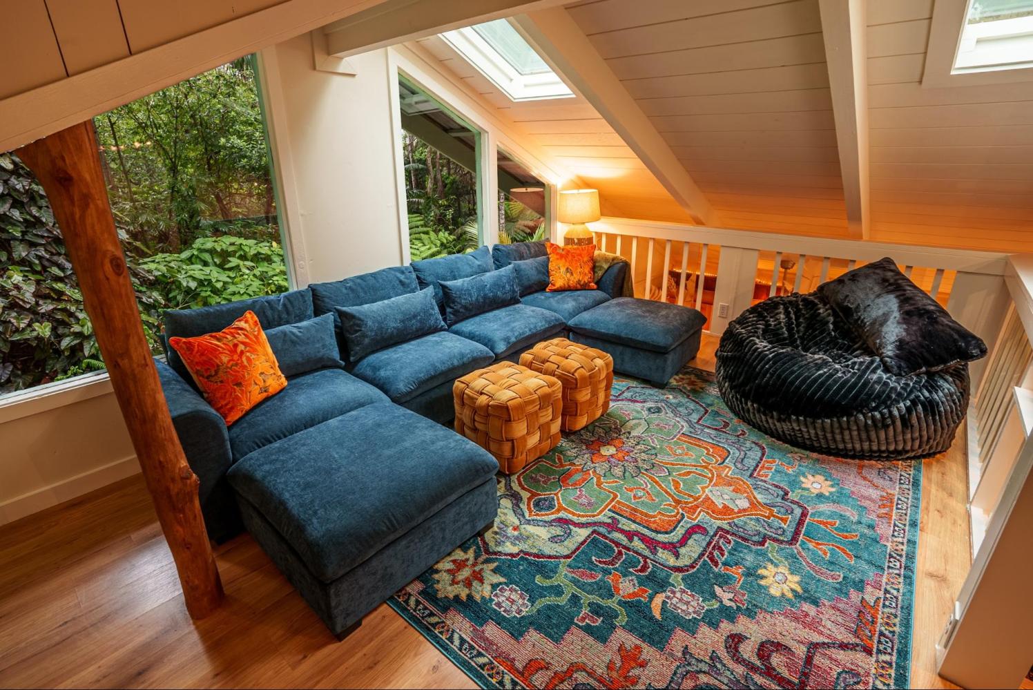 Cozy loft with blue sectional sofa, colorful rug, orange pillows, black bean bag, and skylight.