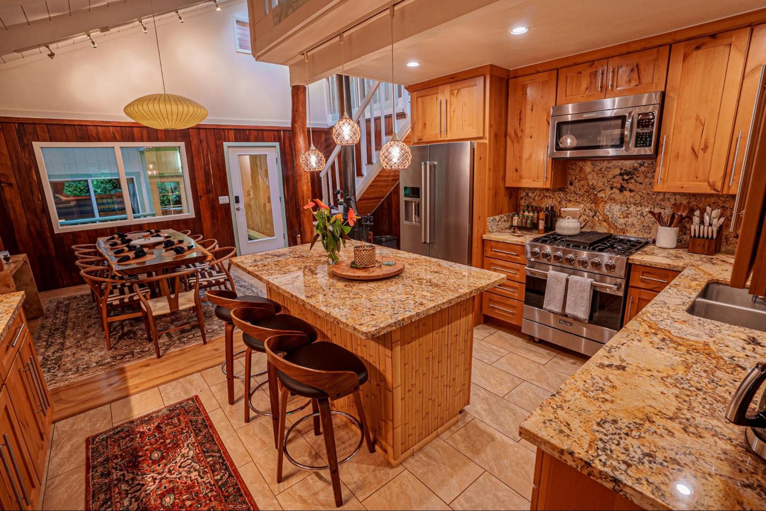 Modern kitchen and dining area with wooden cabinets, marble countertops, and pendant lighting.