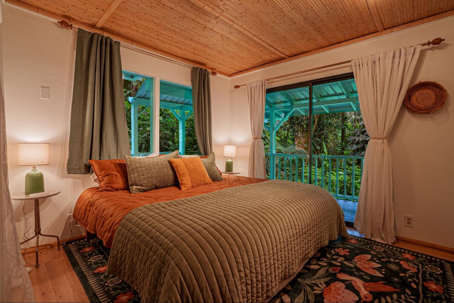 Cozy bedroom with green and orange bedding, lamps, and a view of lush greenery through a sliding door.