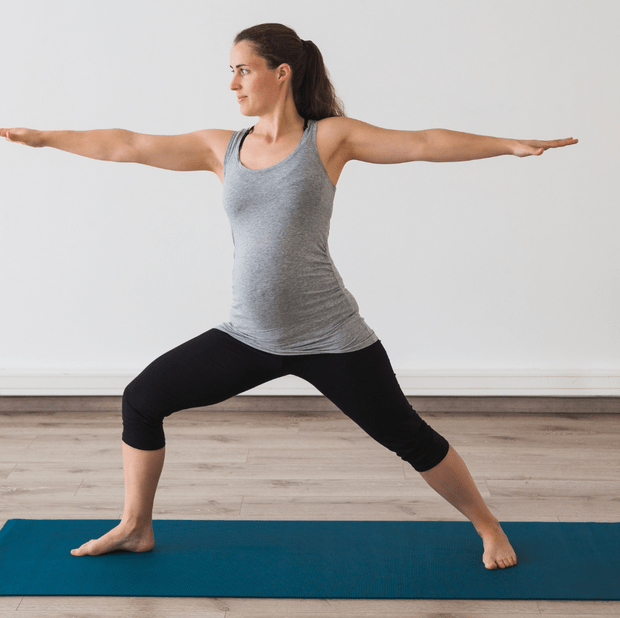 Pregnant woman practicing yoga in warrior pose on a mat.