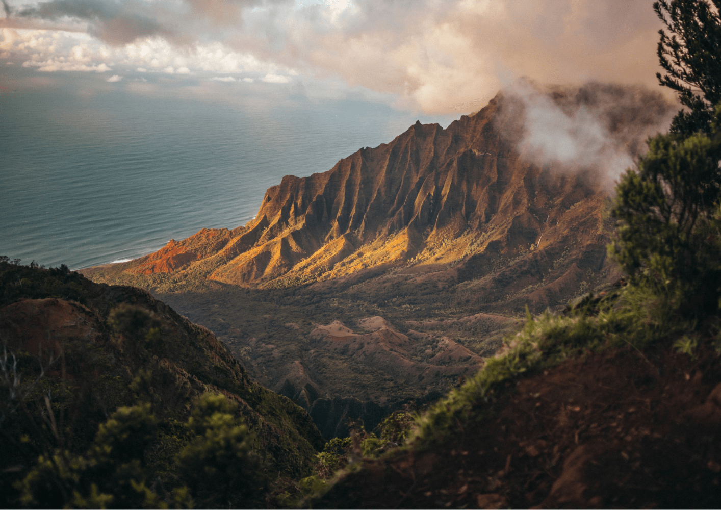 Dramatic mountain range with lush greenery and ocean view under a cloudy sky.