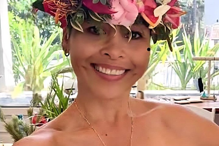 Smiling person wearing a flower crown and a red strapless top outdoors.