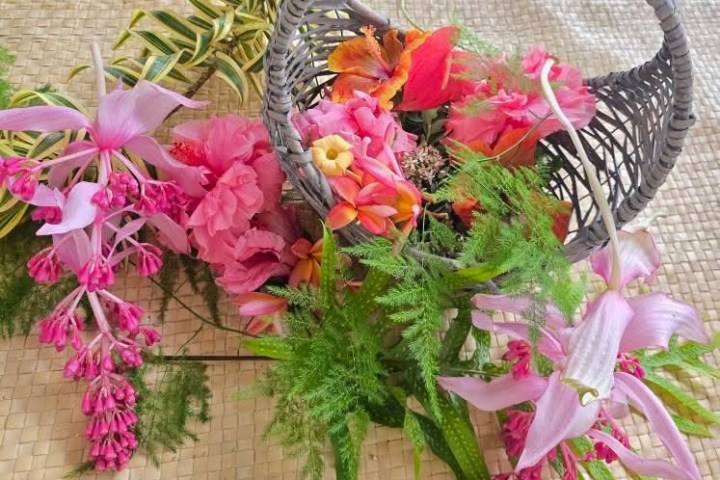 Woven basket spilling vibrant flowers on a straw mat surface.