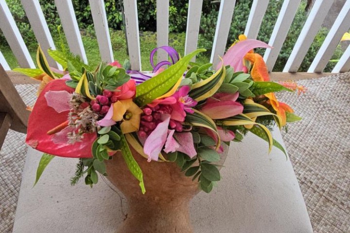 Colorful floral arrangement in a wooden face pot on a cushion.