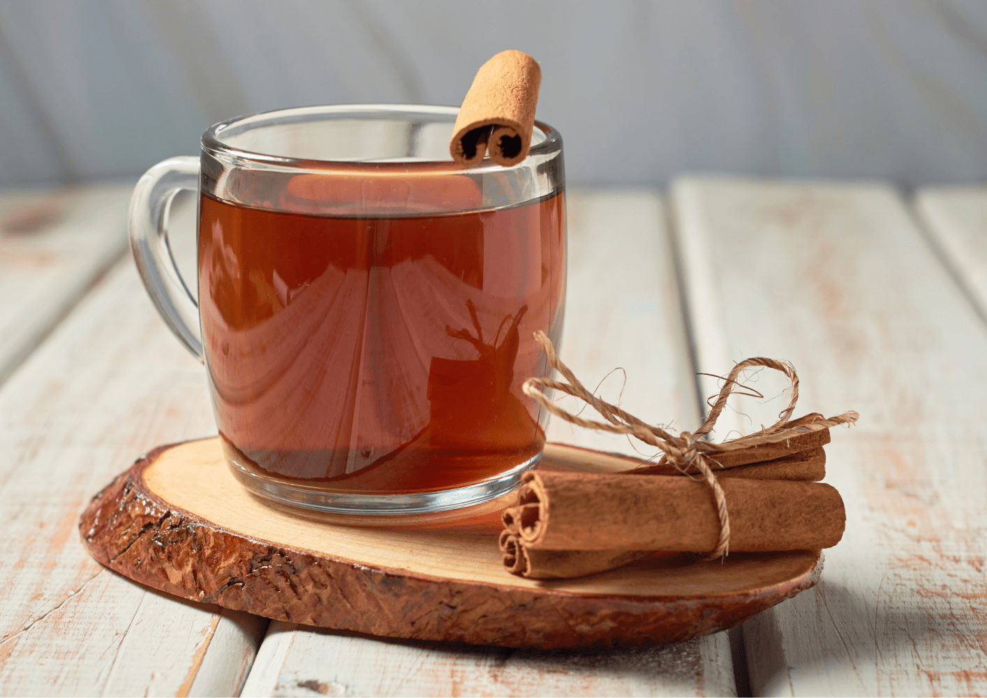 Glass mug of tea with cinnamon stick on wooden slab, tied cinnamon sticks beside.