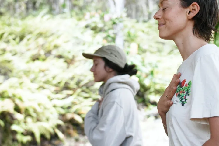 Two people meditating outdoors, one with hand on chest, both in profile view.