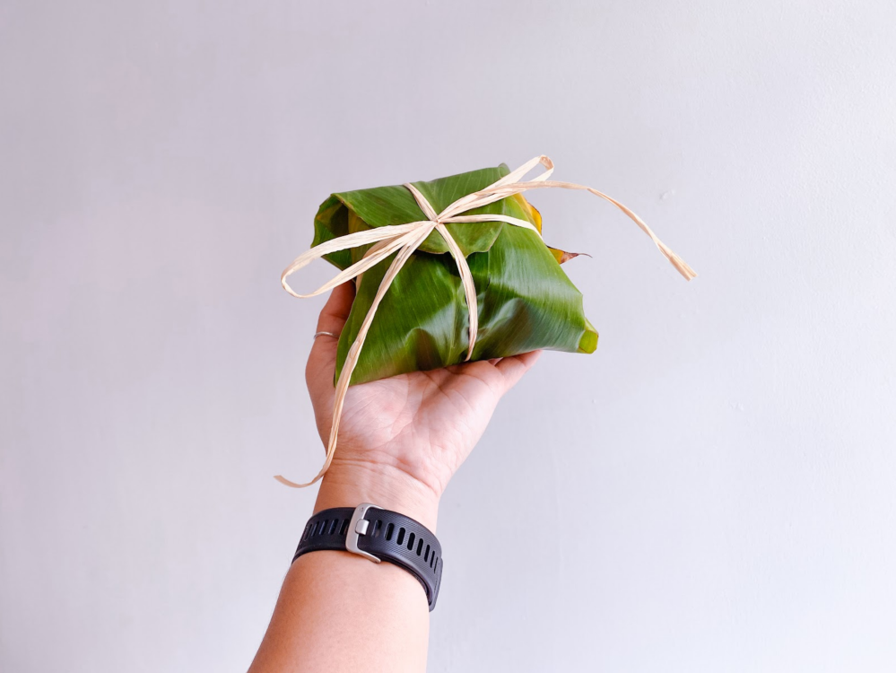 Hand holds a banana leaf-wrapped package tied with a string.