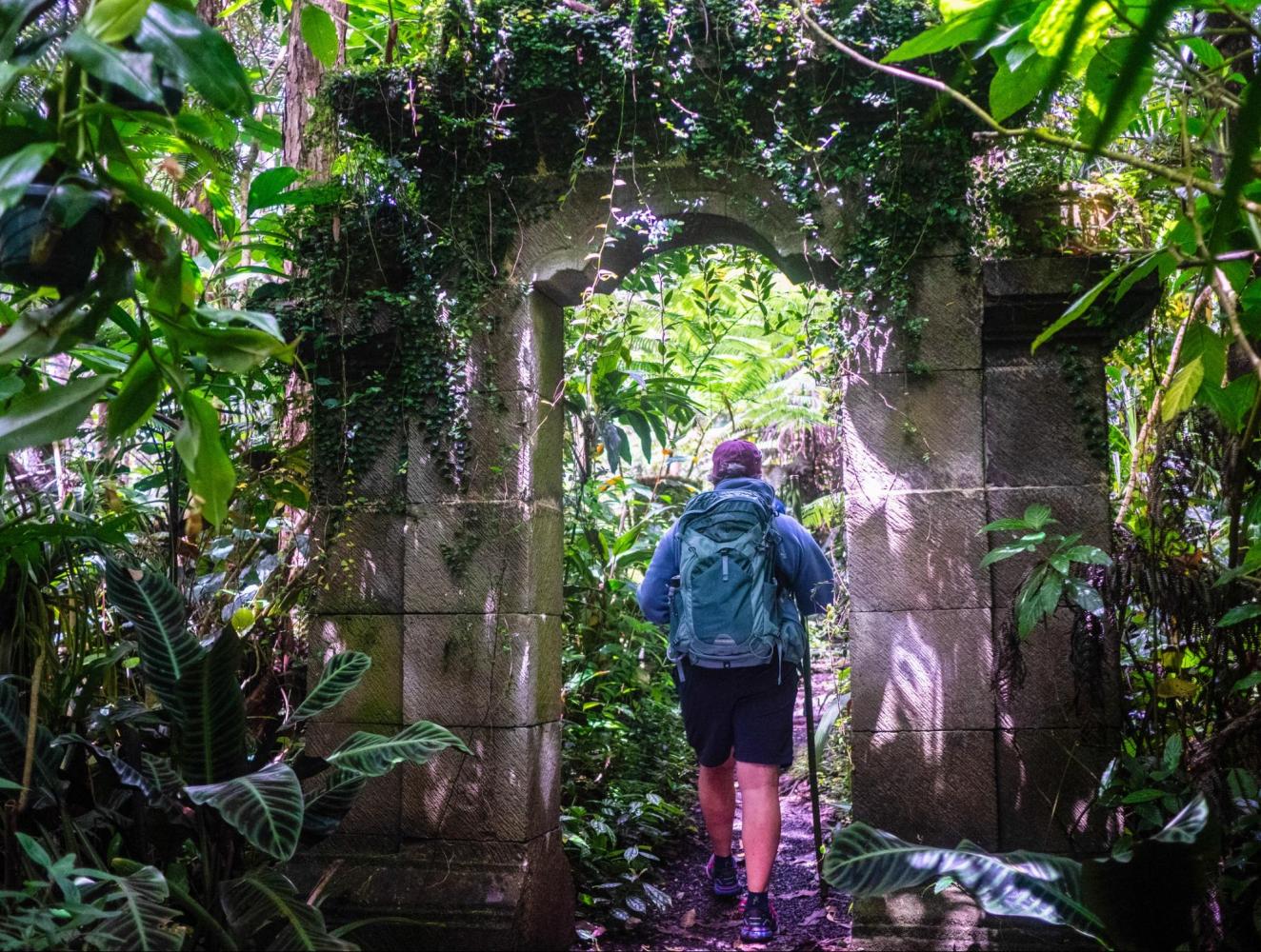 Person with backpack walking through stone arch in lush jungle.