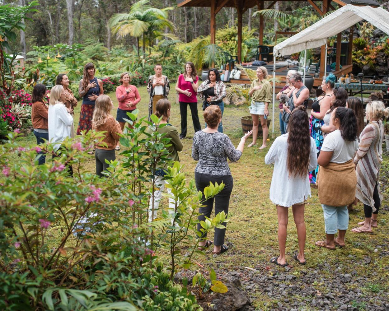 A group of people stands in a circle outdoors in a lush garden setting.
