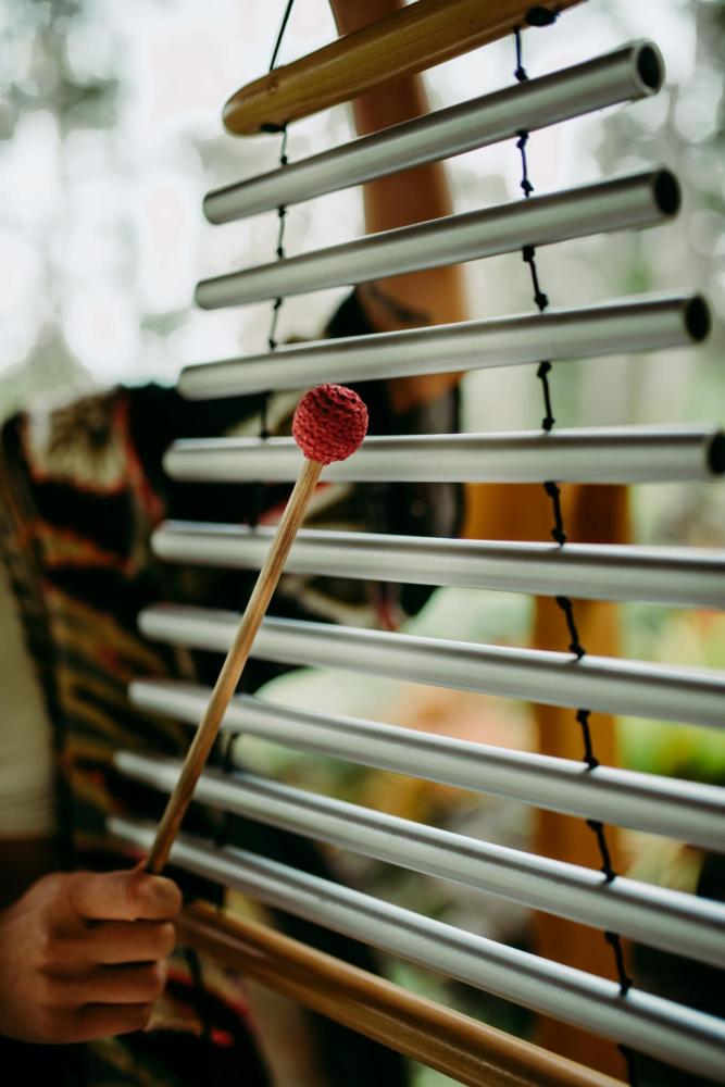 Hand playing metal chimes with a red mallet in a natural setting.