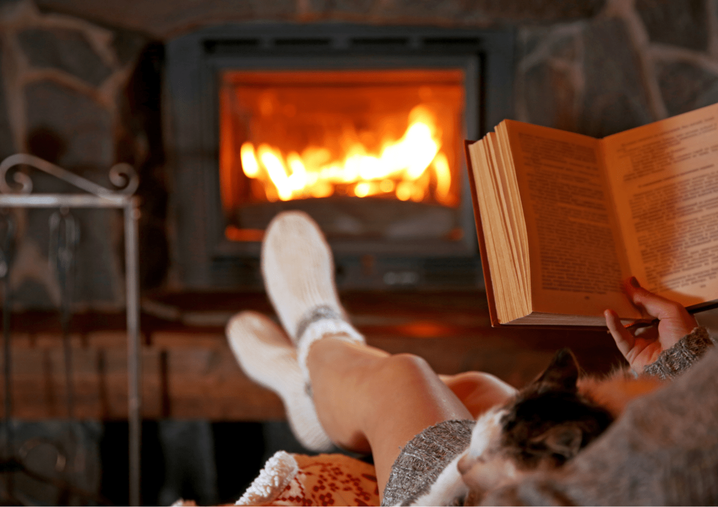Person reading by a cozy fireplace with a cat on their lap.
