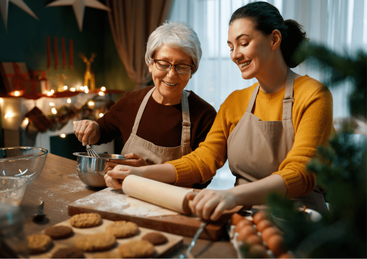 Two women in aprons baking cookies together in a festive kitchen.