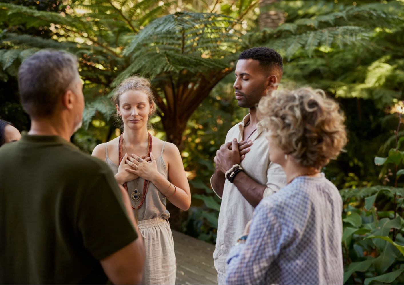 Group of four people meditating outdoors with hands on their hearts.