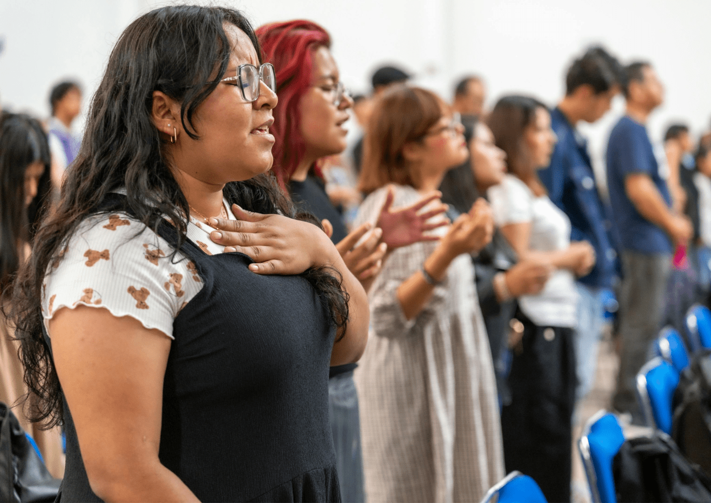 People standing in a room, some with hands on chest and eyes closed.