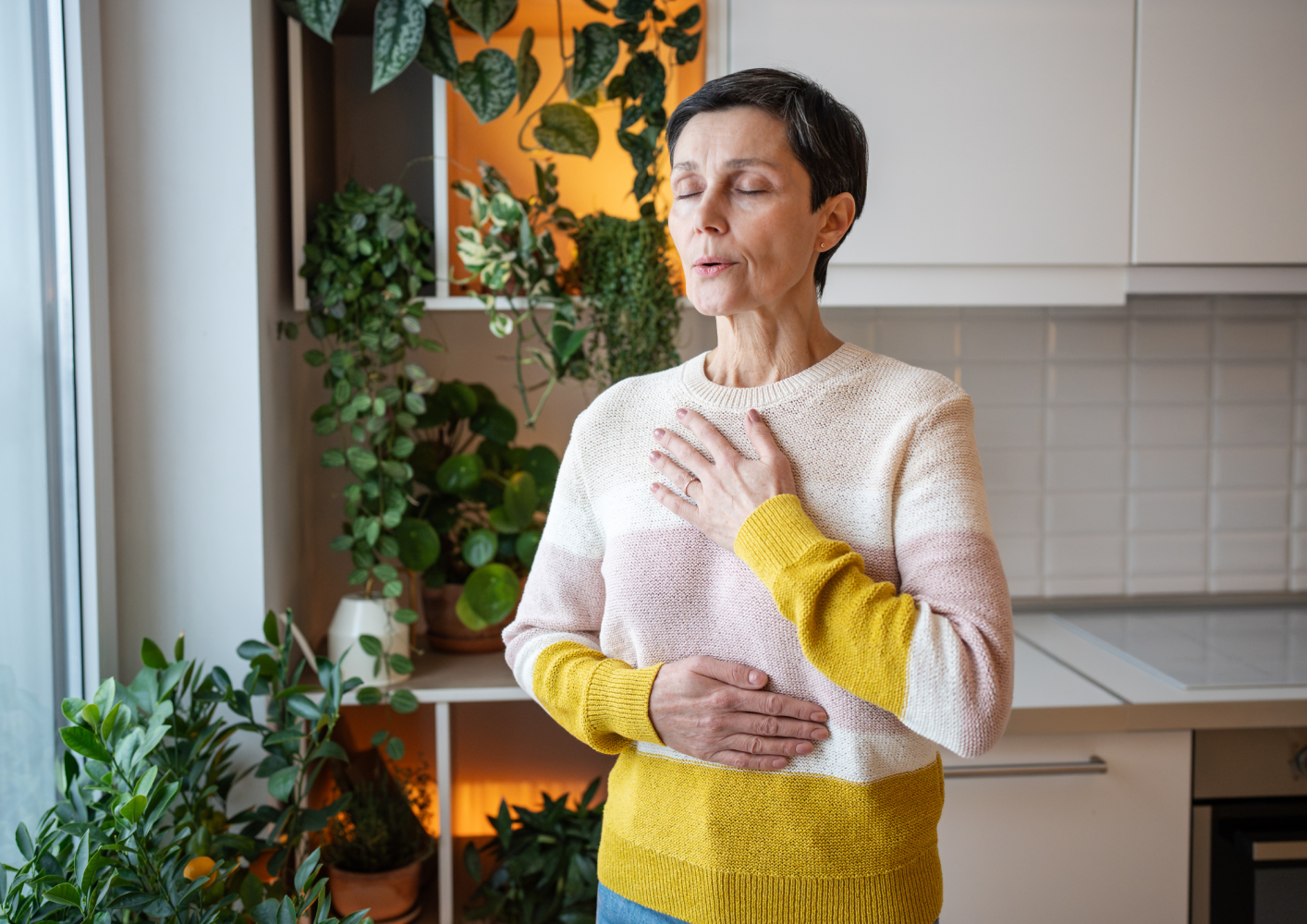 Woman practicing breathing exercises at home with plants in the background.