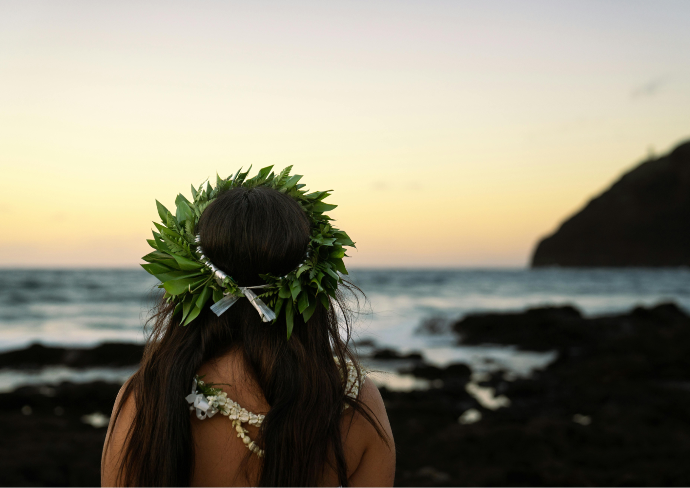 Person with leaf crown views ocean at sunset.