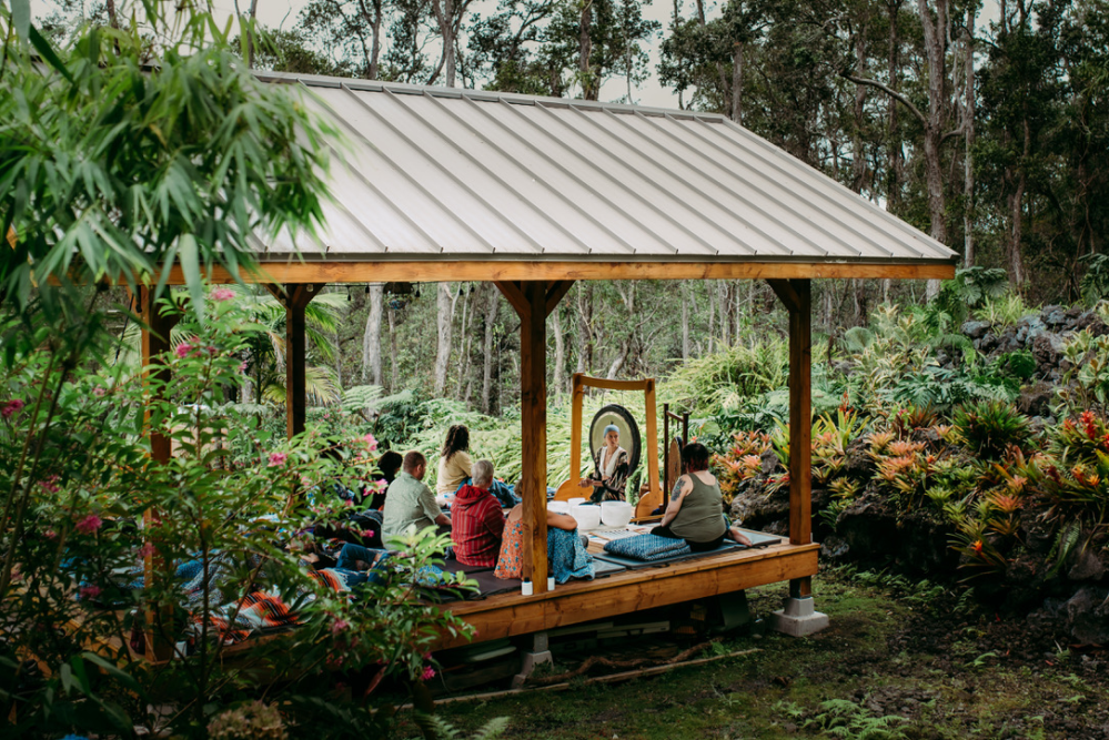 People sitting under a wooden gazebo in a lush garden setting.