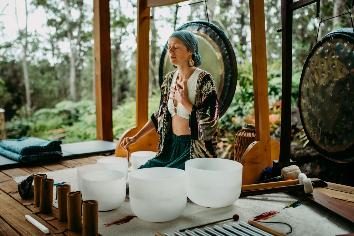 Person meditating with sound bowls and gongs in a forest setting.