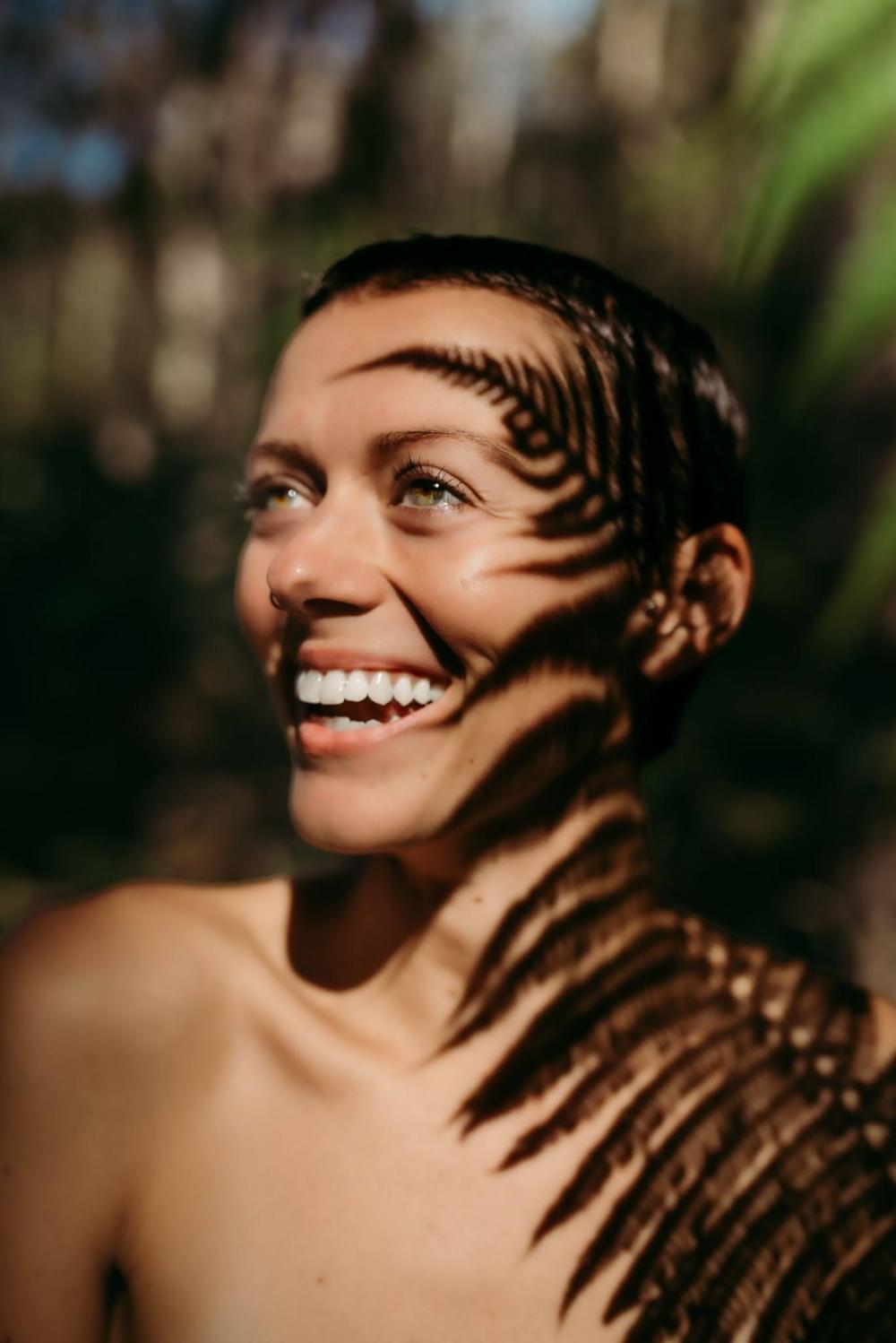 Smiling person with fern shadow across face in outdoor setting.