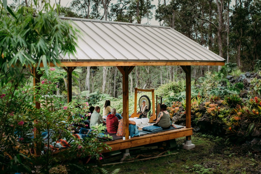 People gathered under a wooden pavilion in a lush forest setting.