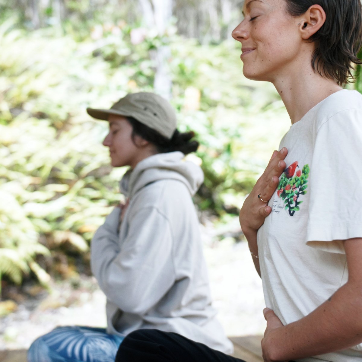 Two people meditating outdoors, hands on chest, eyes closed.
