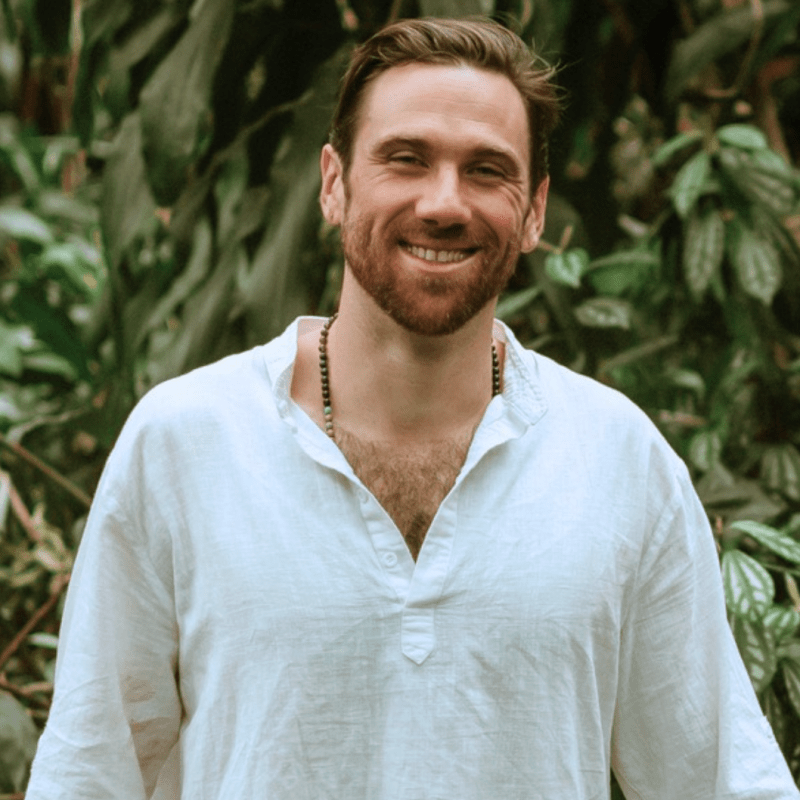 Man in white shirt smiling in front of leafy background
