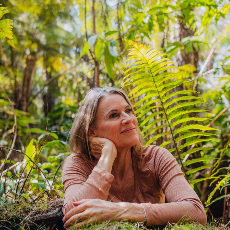 Woman in a forest setting, resting on moss, surrounded by ferns.
