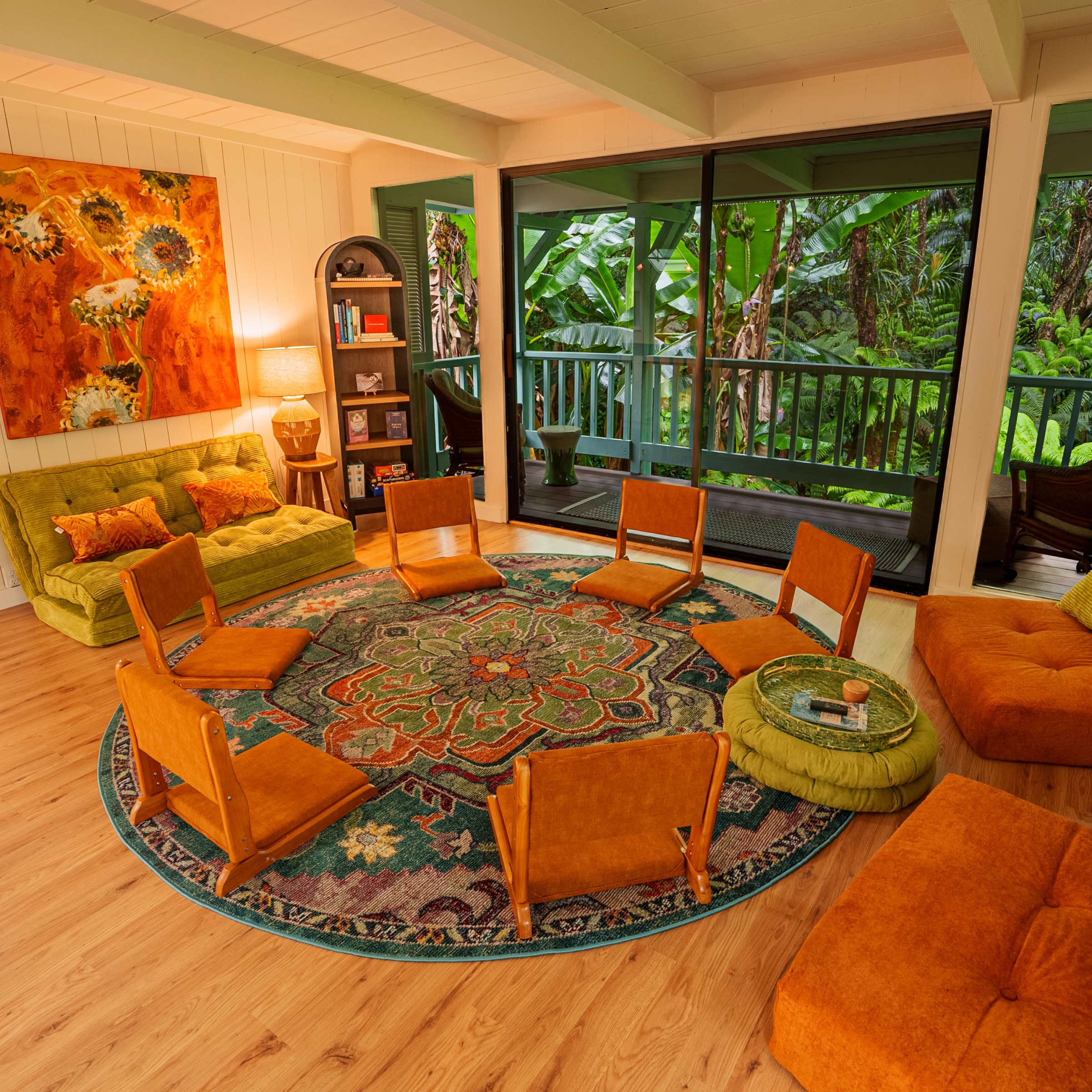 Cozy living room with colorful rug, low chairs, and large window showing lush greenery.