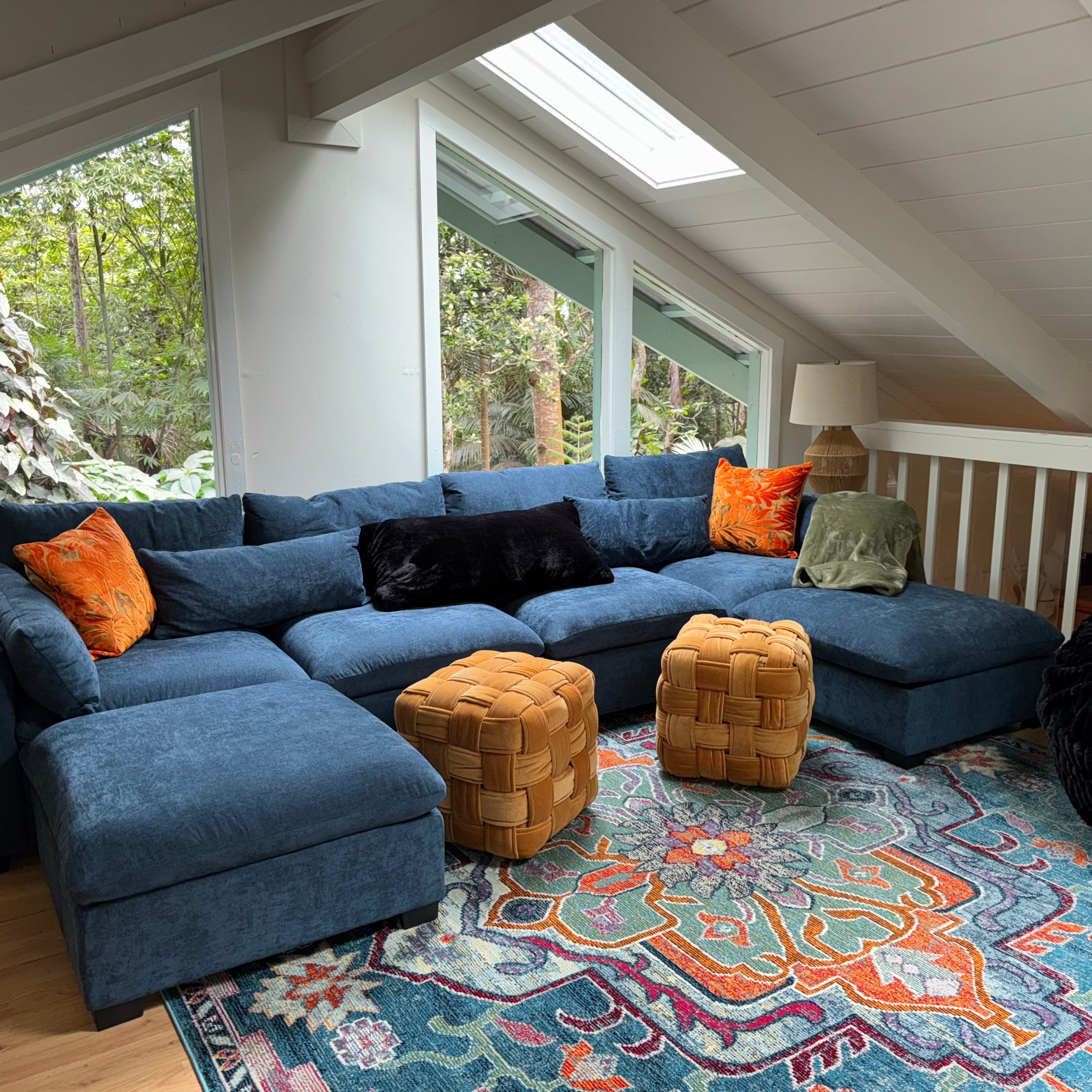 Cozy loft with blue sectional couch, colorful rug, and large windows.